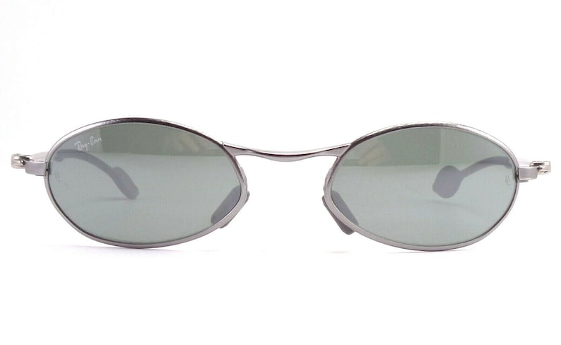 May include: Oval-shaped sunglasses with a silver metal frame and green lenses. The Ray-Ban logo is visible on the left lens. The sunglasses have a classic, minimalist design.