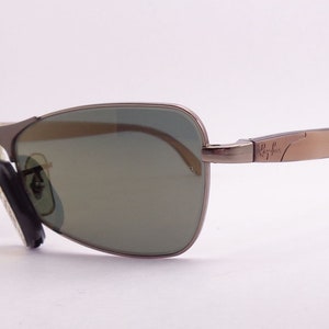 Puede incluir: Un par de gafas de sol con montura de metal marr&oacute;n y lentes verdes. Las gafas tienen el logotipo de Ray-Ban en la patilla derecha.