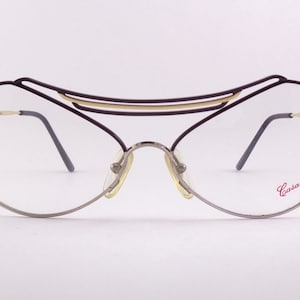 May include: A pair of silver-toned eyeglasses with a black and gold metal frame. The frame has a unique, curved design and the brand name "Casanova" is printed on the right temple.