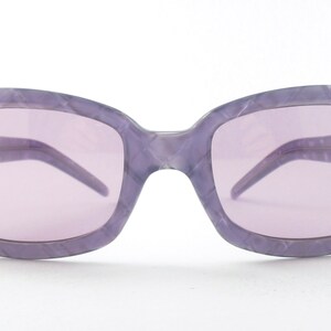 Puede incluir: Gafas de sol moradas con un patrón de mármol en las monturas. Las lentes son de color morado claro.