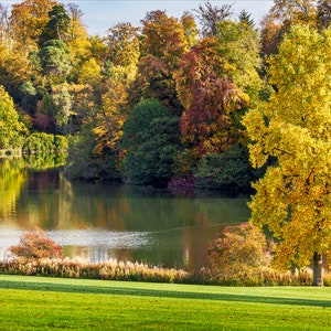 May include: A tranquil lake surrounded by vibrant autumn trees. The leaves are shades of yellow, orange, and red. A small white gazebo can be seen on the left side of the lake.