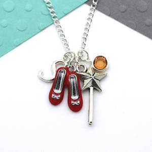 May include: Silver necklace with a red ruby slipper charm, a silver star charm, and a small orange gemstone charm.
