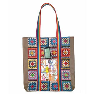 Puede incluir: Una bolsa de mano marrón con correas de arcoíris y un panel frontal de crochet colorido. La bolsa tiene un bolsillo con un teléfono y una revista dentro.