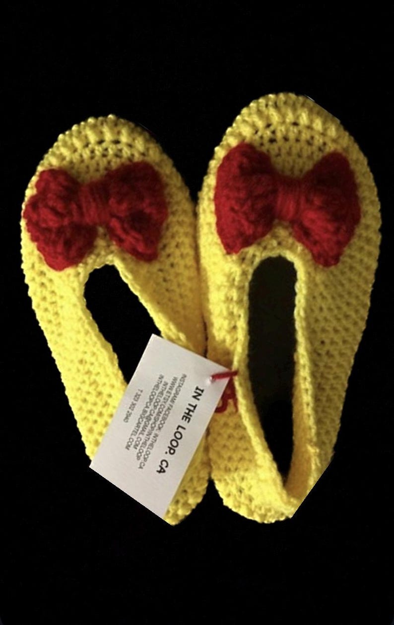 K&ouml;nnte beinhalten: Ein Paar gelbe H&auml;kelpantoffeln mit roten Schleifen. Die Pantoffeln sind handgefertigt und haben ein Etikett mit der Aufschrift "IN THE LOOP. CA".