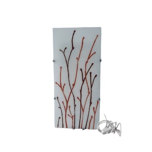 Puede incluir: Una pantalla de lámpara rectangular de vidrio blanco con un diseño de ramas marrones y naranjas. La pantalla está unida a una base de metal plateado.