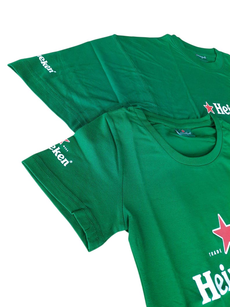May include: Two green t-shirts with the Heineken logo, featuring a red star and white text. The shirts are made of a soft material and have the word "Heineken" printed on the front. The sleeve has the word "Eken" printed on it.