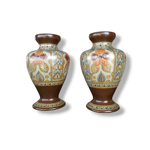 May include: Two brown ceramic vases with white, gold, and orange floral designs. The vases have a wide base and a narrow neck.