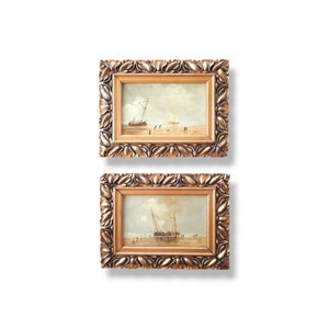 May include: Two framed paintings of seascapes with ships and figures on the shore. The paintings are in gold frames with ornate details.