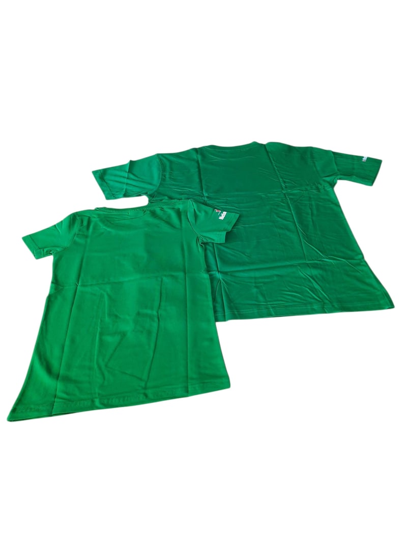 May include: Two green t-shirts, one smaller than the other, are displayed against a white background. The shirts are made of a smooth fabric and have short sleeves. The smaller shirt is in the foreground, with the larger shirt behind it.