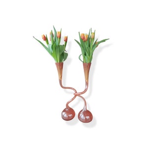 以下が含まれることがあります： 長い曲線状の首を持つオレンジ色のガラスの花瓶2つに、オレンジ色と黄色のチューリップのブーケが活けられています