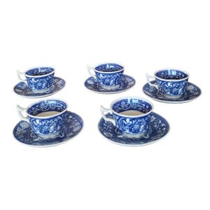 Könnte beinhalten: Ein Set aus fünf blau-weißen Porzellan-Teetassen und Untertassen. Die Tassen und Untertassen weisen ein detailliertes, verziertes Design mit einem Blumen- und Landschaftsmuster auf. Die Tassen haben weiße Griffe.