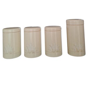 May include: Four beige ceramic canisters with lids. Each canister has a cylindrical shape with a decorative wheat design. The canisters are arranged in a row, varying slightly in height, and are suitable for kitchen storage.