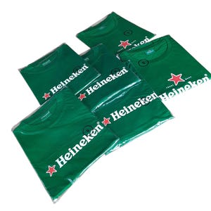 May include: Several green t-shirts, each packaged in clear plastic. The shirts feature the Heineken logo in white with a red star. The shirts are a solid green color.
