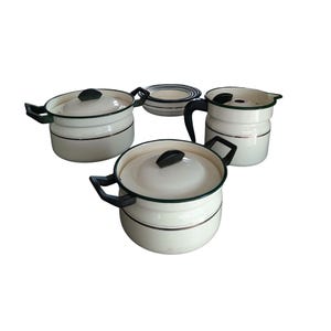 May include: A set of vintage cream-colored enamelware cookware with black handles and green trim. The set includes two lidded pots, a pitcher, and a small bowl. The cookware has a classic, retro design.