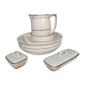 May include: A vintage cream-colored porcelain wash set with gold trim. The set includes a pitcher, a small bowl, a large basin, and two lidded containers. The pieces are arranged on a white background.