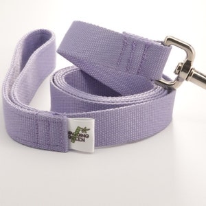 May include: A lavender dog leash with a silver metal clasp. The leash is made of a durable, woven material and features a loop handle. A white tag with green text is attached to the leash.