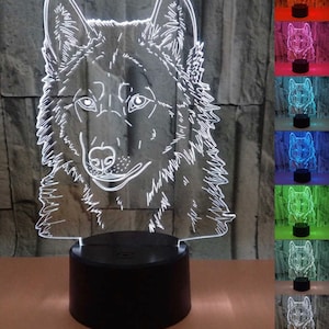May include: A 3D printed wolf head night light with a black base. The light is illuminated in white, but can change colors. The image shows the light in various colors, including red, blue, green, and purple.