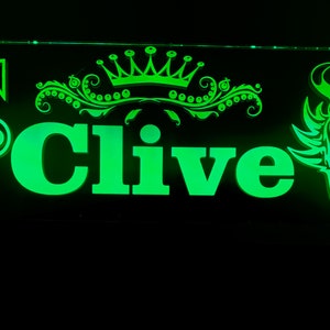 Może przedstawiać: Zielony podświetlany znak z logo Volvo, koroną, imieniem Clive i grafiką wikinga. Znak wykonany jest z przezroczystego akrylu.