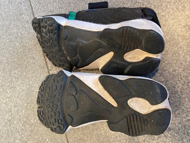 Pu&ograve; includere: Un paio di scarpe da ginnastica nere e bianche con una suola spessa. Le scarpe da ginnastica hanno un cinturino verde sulla parte superiore.