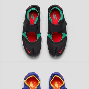 Pu&ograve; includere: Due paia di sandali Nike Air Rift Original. Il primo paio &egrave; nero con accenti rossi, verdi e bianchi. Il secondo paio &egrave; blu con accenti gialli, rossi e bianchi.
