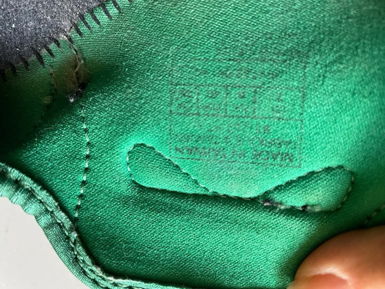 Pu&ograve; includere: Primo piano dell'interno di una scarpa verde con cuciture nere e un'etichetta nera che recita "MADE IN CHINA  ALL MATERIALS  ARTIFICIAL DOWN"
