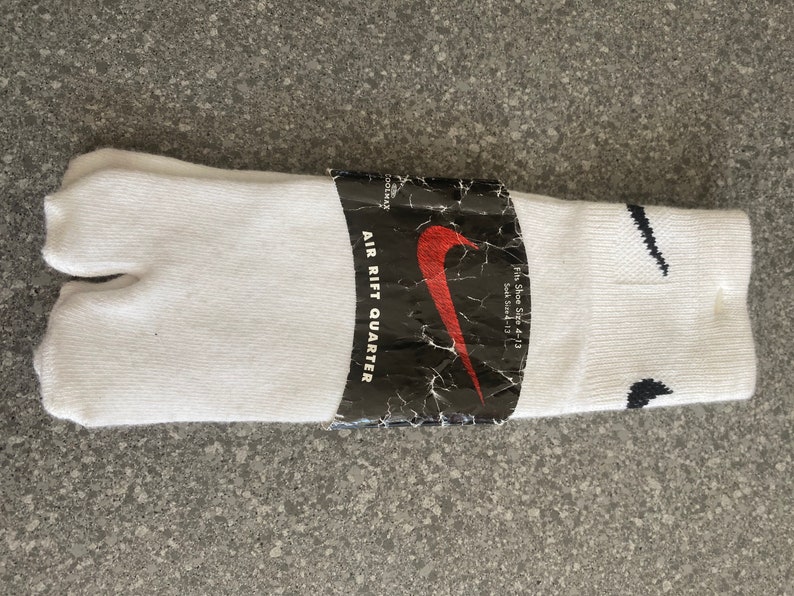 Pu&ograve; includere: Calzini tabi bianchi con un logo Nike swoosh nero e il testo "AIR RIFT QUARTER" sulla confezione. La confezione indica anche "Fit Shoe Size 4-13 Sock Size 13".