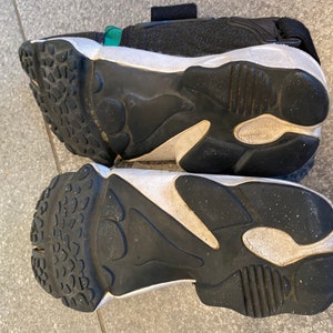 Pu&ograve; includere: Un paio di scarpe da ginnastica nere e bianche con una suola spessa. Le scarpe da ginnastica hanno un cinturino verde sulla parte superiore.