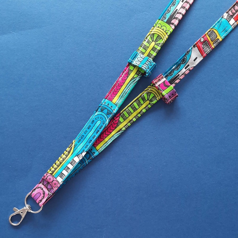 A fun fabric lanyard with a colourful funky rainbow design. A camper van appears occasionally across the print. The lanyard has a loop on each strap with a pair of glasses held in one loop and a pen in the other.