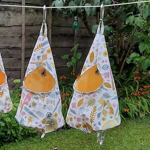 PDF Sewing pattern for a peg bag (clothespin bag). The photo shows the to sizes of bag handing from a washing line by a carabiner. Conical shape with a large hole for your hand to fit in. There are 2 sizes Extra Large & XXL and a YouTube tutorial.