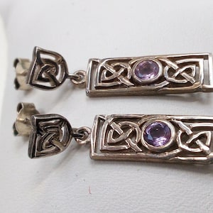 May include: A pair of silver earrings featuring a Celtic knot design with a purple gemstone at the centre of each earring.