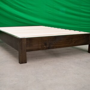 May include: A dark brown wooden bed frame with a slatted base. The frame has a simple, modern design with square legs.