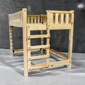 May include: A light-colored wooden loft bed frame featuring a tall, integrated ladder on the front side. The structure is built with vertical slats along the upper guardrails and sturdy corner posts, providing an open, elevated sleeping platform.