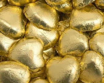 May include: A close-up of a pile of gold foil-wrapped chocolate hearts. The hearts are arranged in a random pattern, creating a visually appealing and festive display.