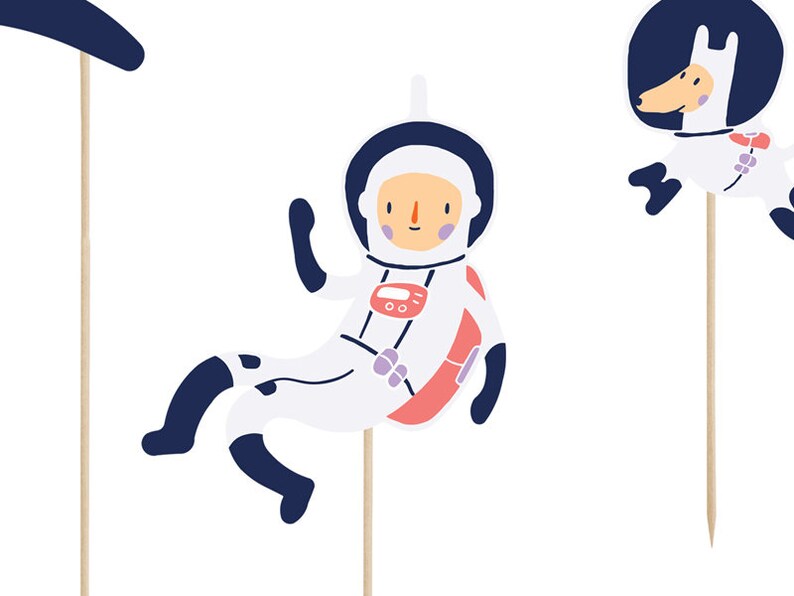 May include: A set of three astronaut-themed cake toppers. The toppers feature a white astronaut with a red and pink spacesuit, a white dog with a blue space helmet, and a blue crescent moon.