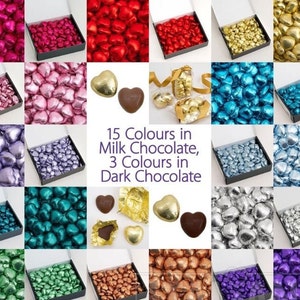 May include: An assortment of heart-shaped chocolates in various colours, including pink, red, gold, blue, silver, teal, green, copper, and purple. The chocolates are arranged in boxes and displayed on a white background. The text "15 Colours in Milk Chocolate, 3 Colours in Dark Chocolate" is displayed in the centre of the image.