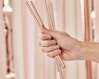 May include: A set of six rose gold reusable drinking straws. The straws are made of metal and are held in a hand.