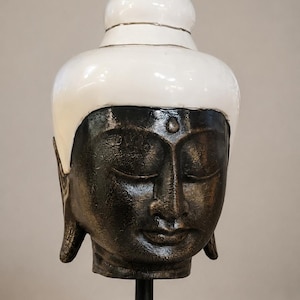 Large Buddha head on a black wooden base, heavy Asian sculpture in bronze finish with a white pointed cap, total height 40 cm.
