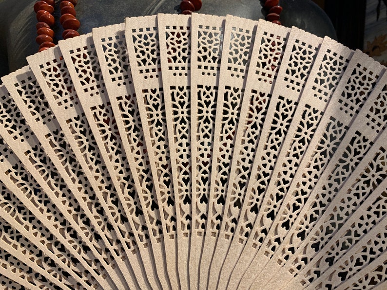 May include: A white folding fan with intricate cut-out designs. The fan is made of thin, delicate wood and has a traditional Asian style.