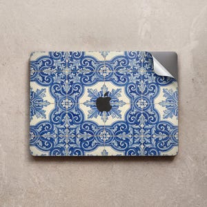 Peut inclure: Une peau d'ordinateur portable ornée d'un motif de carreaux bleus et blancs, rappelant les carreaux azulejos portugais traditionnels. Le design comprend des motifs floraux et géométriques. Le logo Apple est visible.