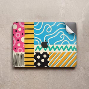 May include: A laptop skin featuring a vibrant collage of patterns including pink circles, black horizontal stripes, blue squiggles, a green zigzag line, black polka dots on white, and yellow diagonal stripes, with a central black Apple logo.