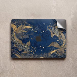 May include: A navy blue laptop skin featuring a gold koi fish design. The illustration shows two koi fish swimming in opposite directions, surrounded by gold swirls and water patterns. The Apple logo is visible.