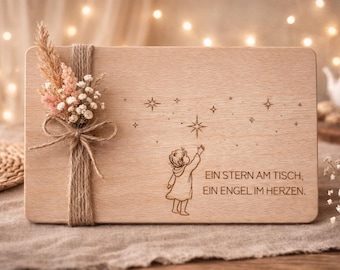 May include: A rectangular wooden plaque with a floral arrangement and twine. The plaque features an engraved illustration of a child reaching for a star, with the text "EIN STERN AM TISCH, EIN ENGEL IM HERZEN."