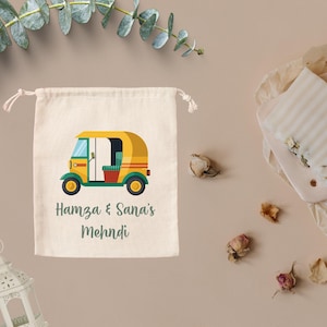 May include: A white cotton drawstring bag with a yellow and green auto rickshaw illustration and the text "Hamza & Sana's Mehndi".