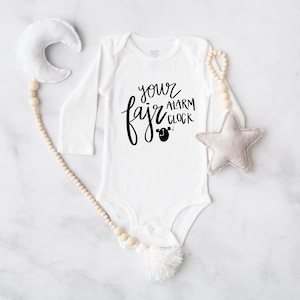 May include: White long-sleeved baby onesie with black text that reads "your fajr alarm clock" and a small black alarm clock graphic.