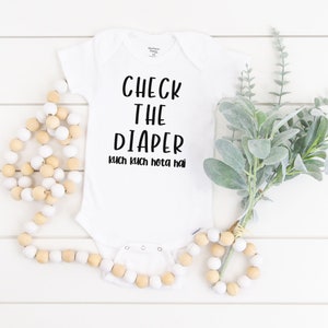 May include: White baby onesie with black text that reads "Check the Diaper kuch kuch hota hai".