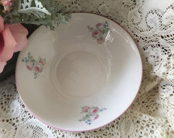 May include: A white ceramic bowl with a pink rim and floral designs. The bowl features pink roses and blue flowers.