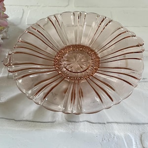 May include: A pink glass serving dish with a scalloped edge and a fluted center. The dish has two handles on the sides.