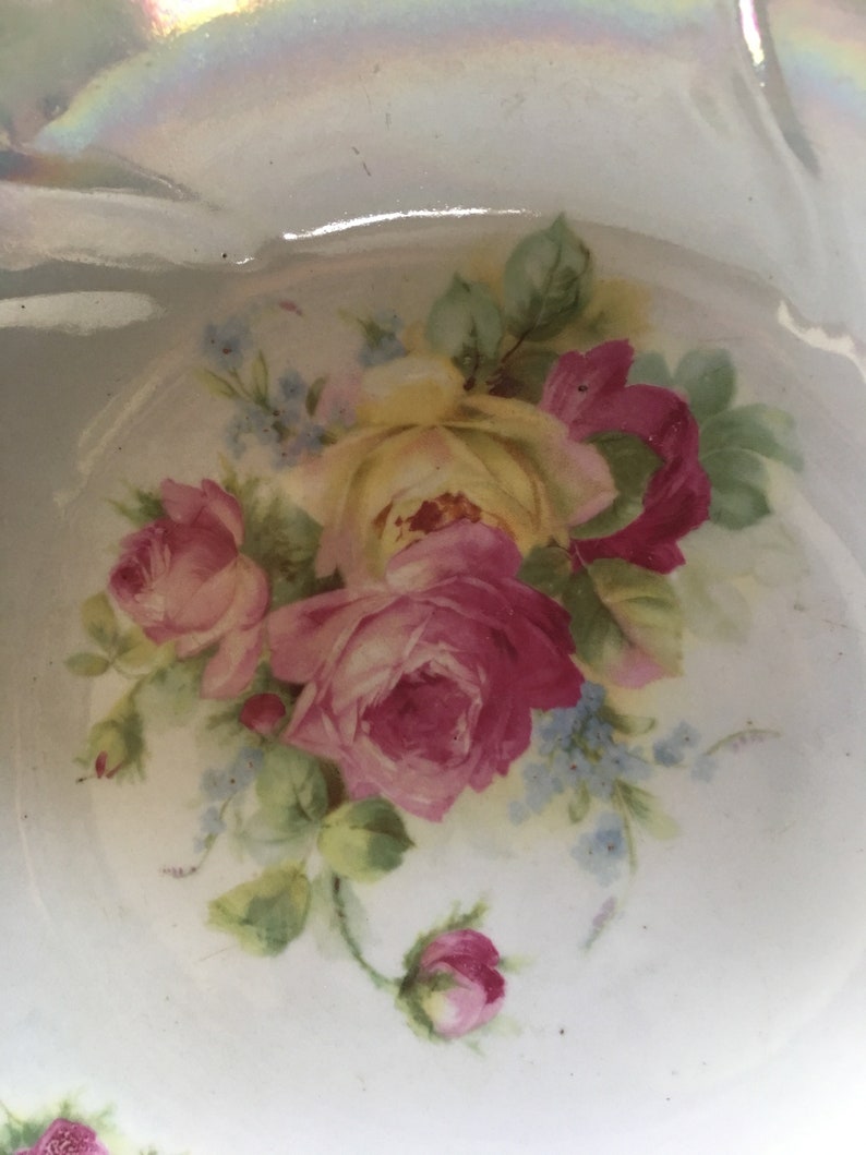 K&ouml;nnte beinhalten: Eine wei&szlig;e Porzellanschale mit einem Blumendesign aus rosa und gelben Rosen und blauen Vergissmeinnicht. Die Schale hat einen gewellten Rand und eine gl&auml;nzende Oberfl&auml;che.