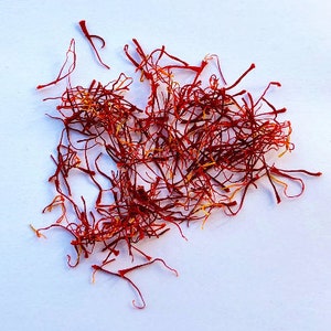 May include: A pile of dried saffron threads, a vibrant red-orange color, on a white background.
