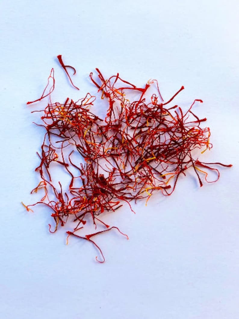 May include: A pile of dried saffron threads, a vibrant red-orange color, on a white background.